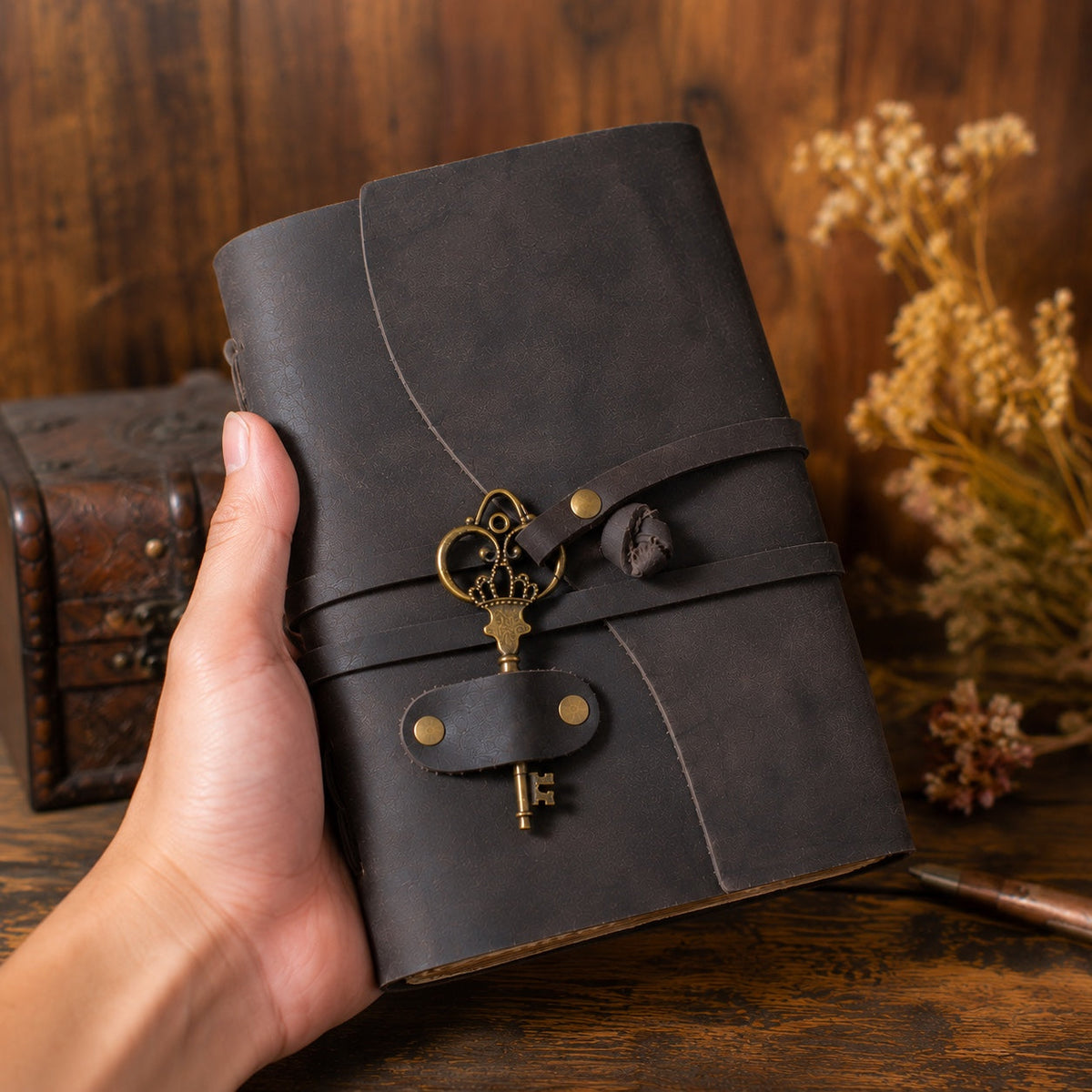 Hand holding dark leather journal showing its size and closure